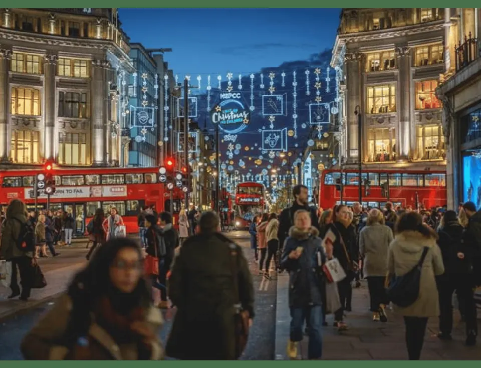 Busy London shopping street with Christmas decorations, illuminated shopfronts and red buses
